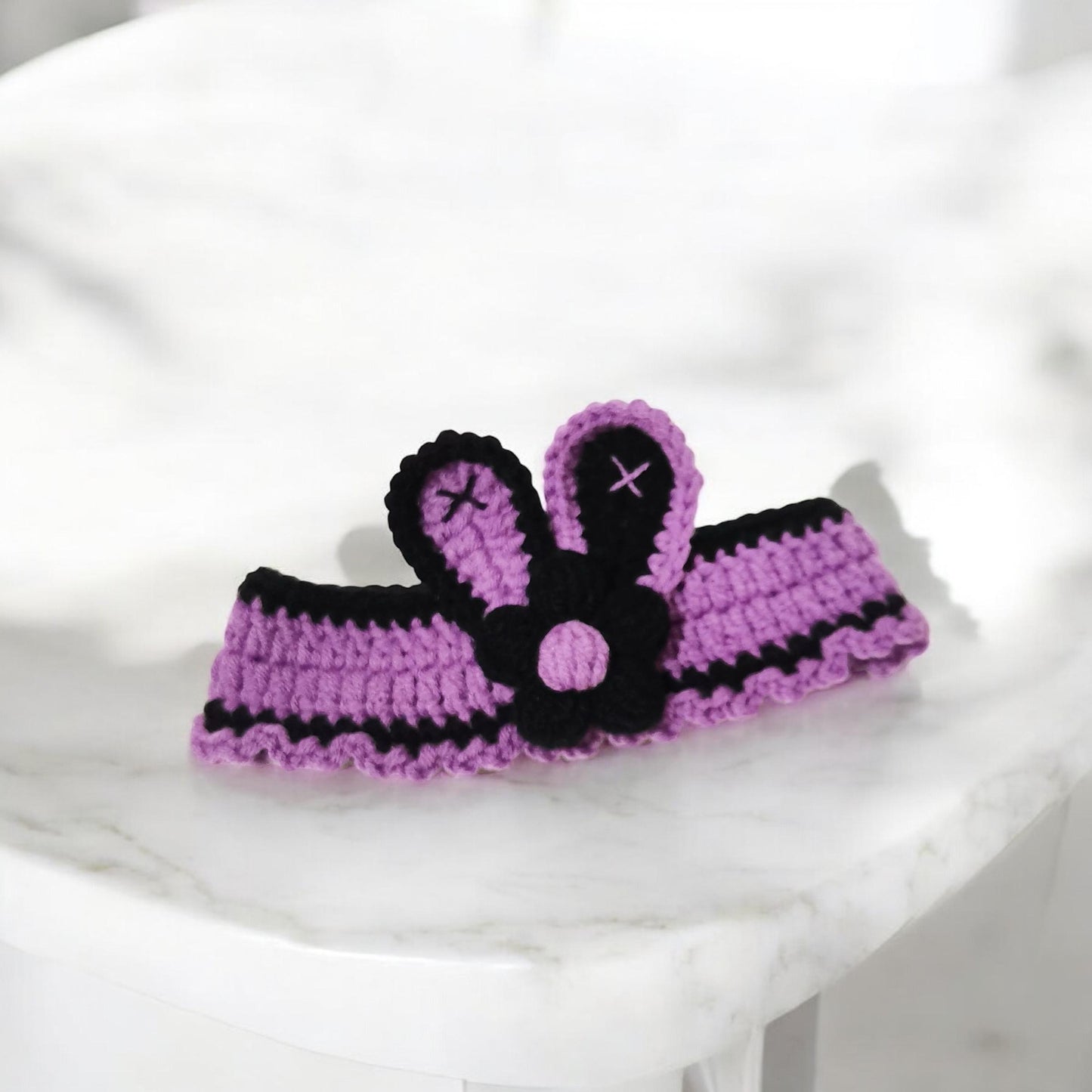 Crocheted pet collar featuring patterns in purple color with decorative flower and bunny ears in the center.