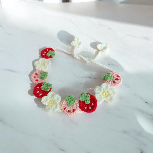 A crocheted pet collar featuring flowers and strawberries in vibrant colors such as red, white, and pink.